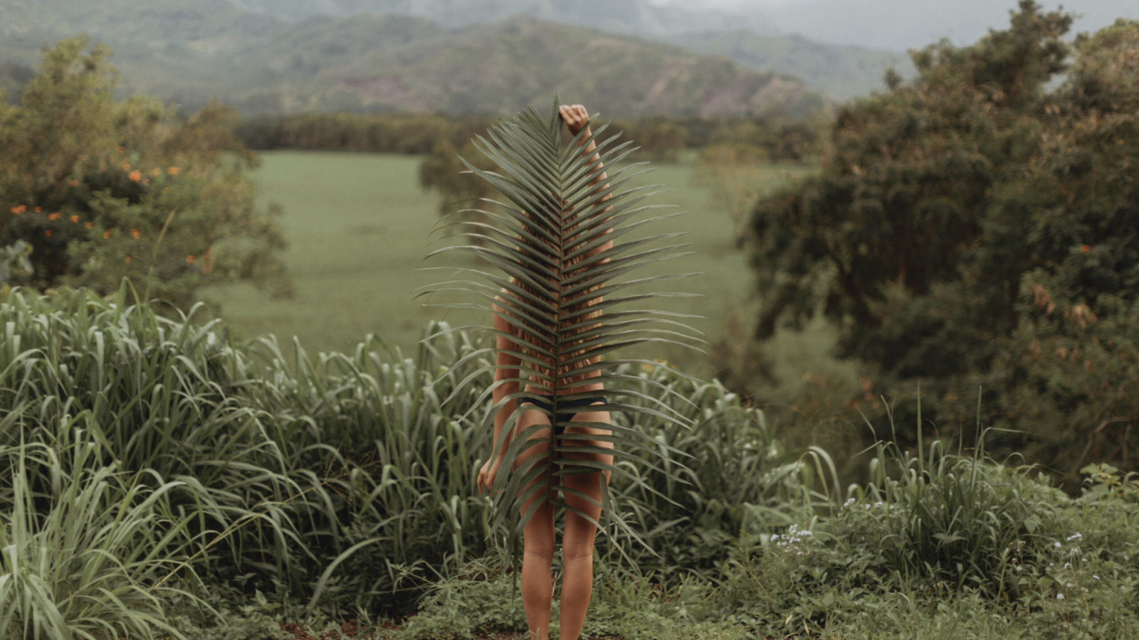 Woman in a bikini holding a large leaf in the jungle, symbolising raw instinct and nature before civilisation